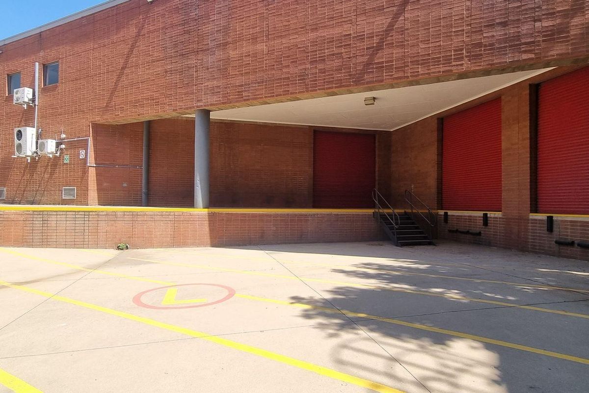 Commercial loading bay area featuring a brick facade, multiple red roller shutter doors, and a raised concrete platform for efficient logistics and freight access.