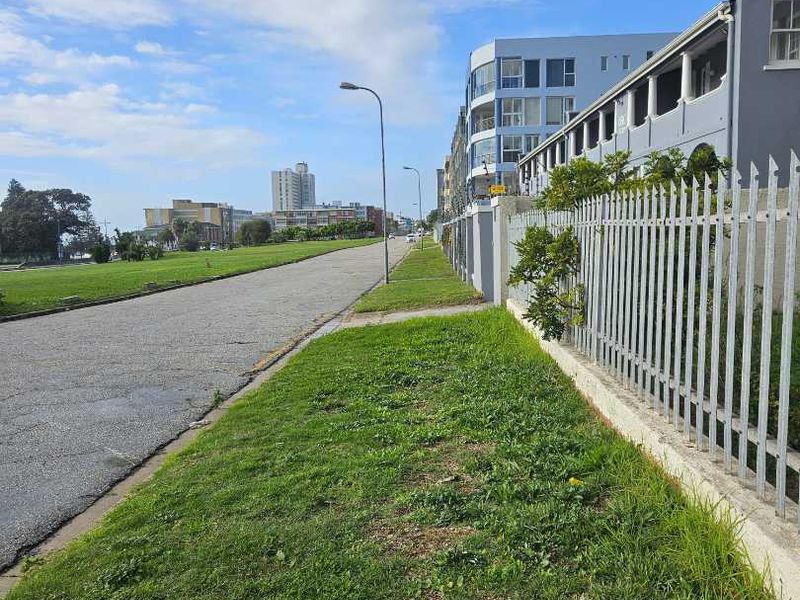 A street-level view showing the exterior perimeter fencing of the apartment complex and the adjacent road and grass verge.