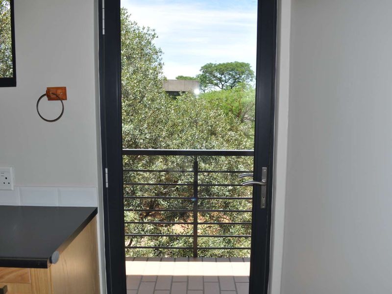 A bright office space featuring a modern black-framed door leading to a private balcony with a metal balustrade and views of surrounding trees.