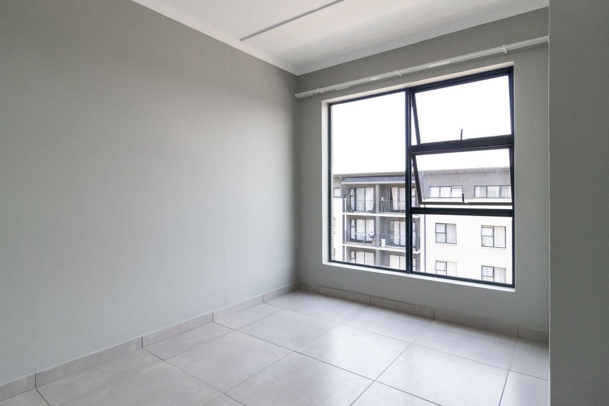 A bright, empty bedroom featuring neutral grey walls, large aluminium-framed windows, and clean tiled flooring, ready for personalization.