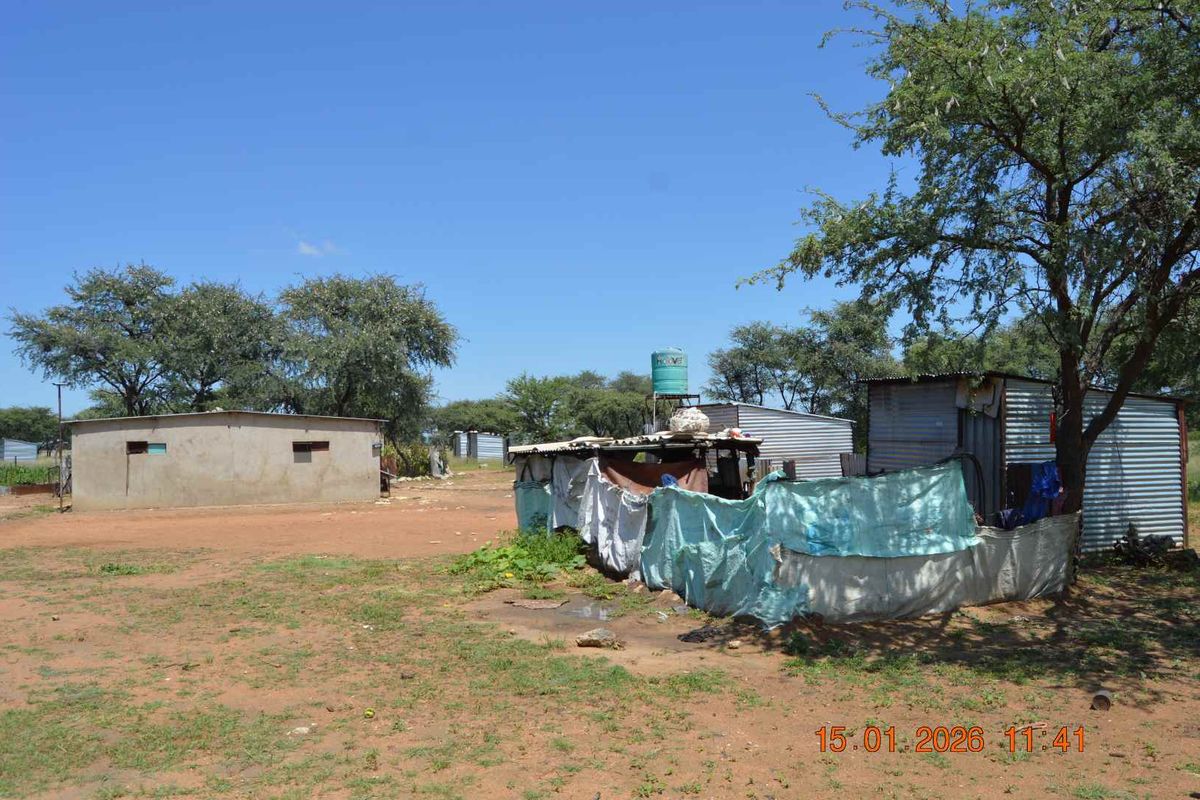 A rural farm property featuring multiple basic corrugated metal structures and a water storage tank on a large, unpaved plot of land.