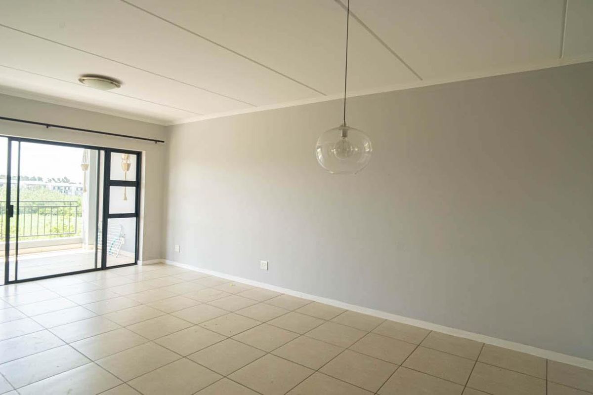Spacious living area featuring neutral tiled flooring, a modern pendant light fixture, and large sliding glass doors providing access to an outdoor balcony.