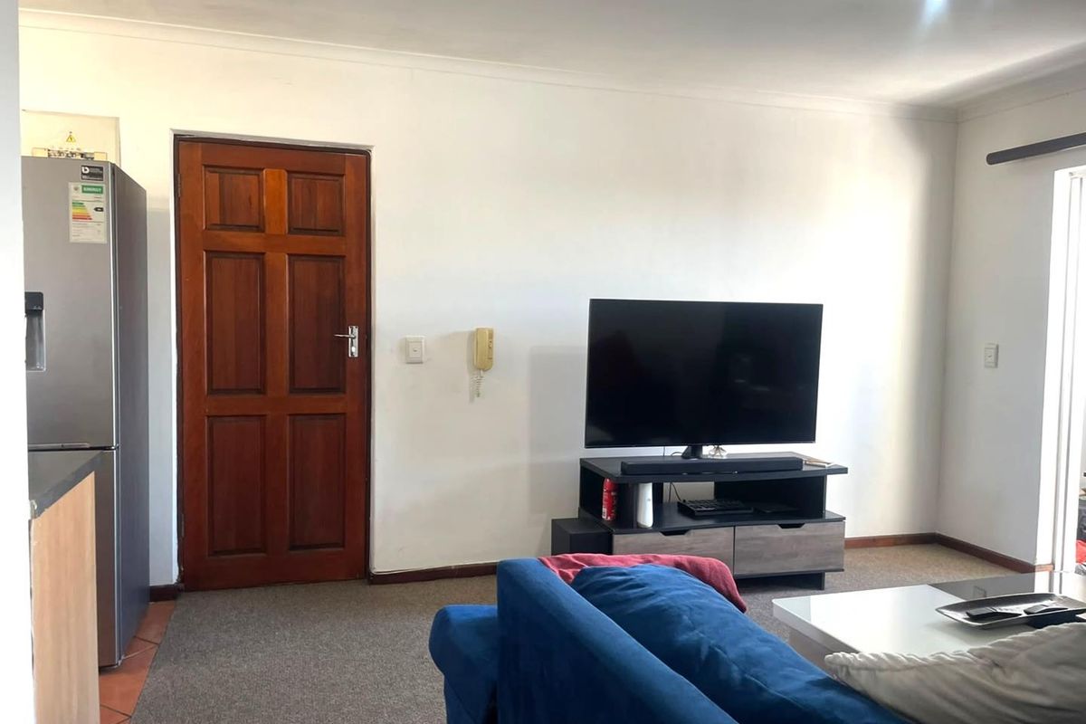 A living room area featuring carpet flooring, coving, and a wall-mounted intercom system.