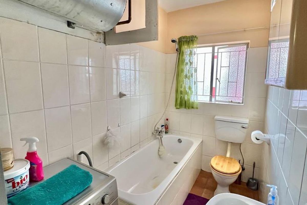 Compact bathroom featuring a bathtub, toilet, and basin, with an integrated laundry area and exposed water heating infrastructure.