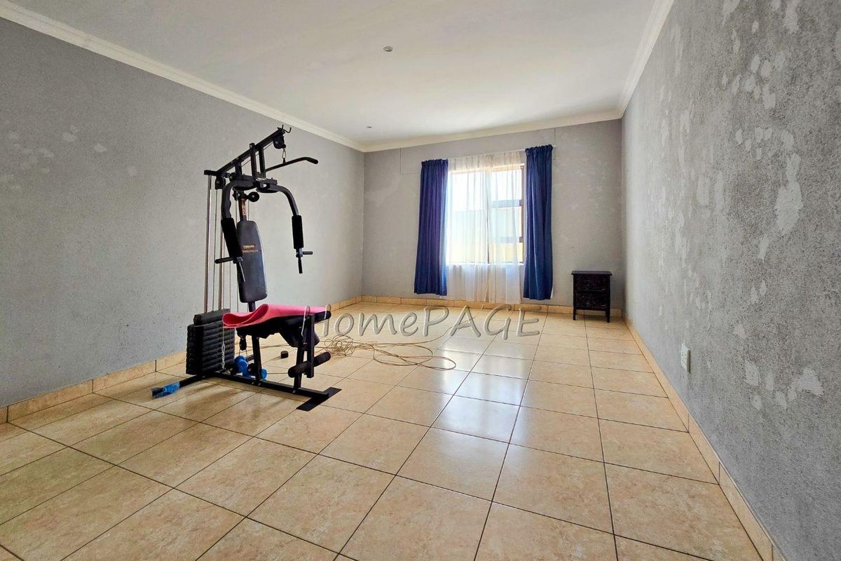 A spacious, tiled bedroom featuring neutral grey walls and a window with curtains, offering a blank canvas for personalization.