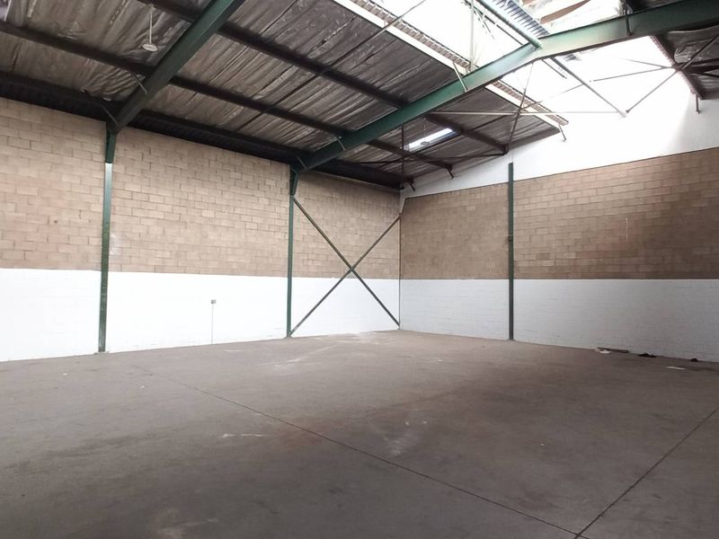 Spacious industrial warehouse unit featuring high ceilings, exposed steel structural beams, concrete flooring, and blockwork walls with natural light from roof panels.
