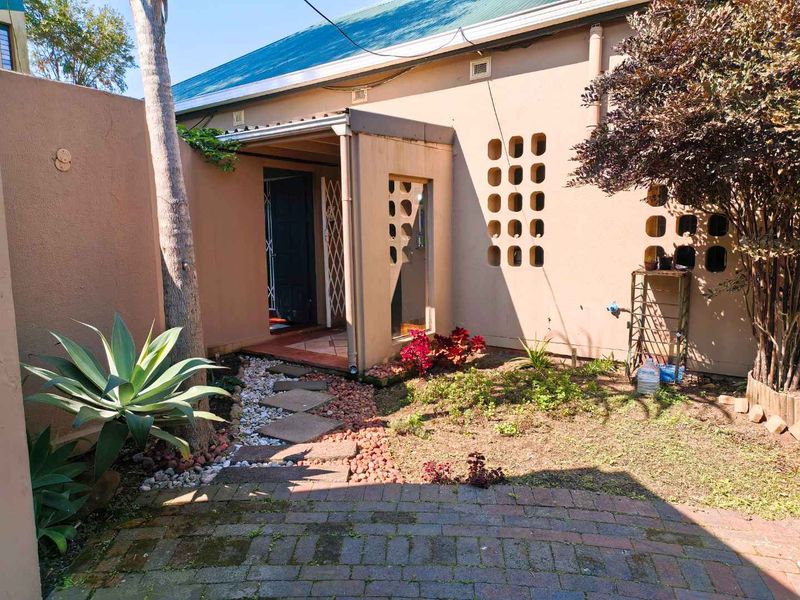 Rear exterior view of the townhouse featuring a paved walkway, covered entrance with security gate, and decorative breeze block wall detailing.