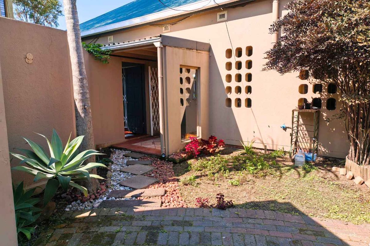Rear exterior view of the townhouse featuring a paved walkway, covered entrance with security gate, and decorative breeze block wall detailing.