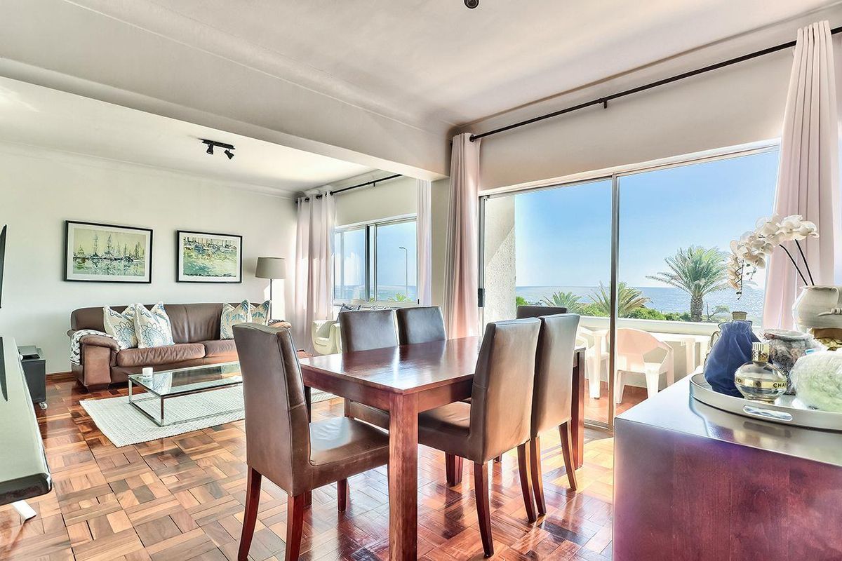 Spacious open-plan living and dining area featuring beautiful parquet flooring and large sliding glass doors that open onto a balcony with ocean views.