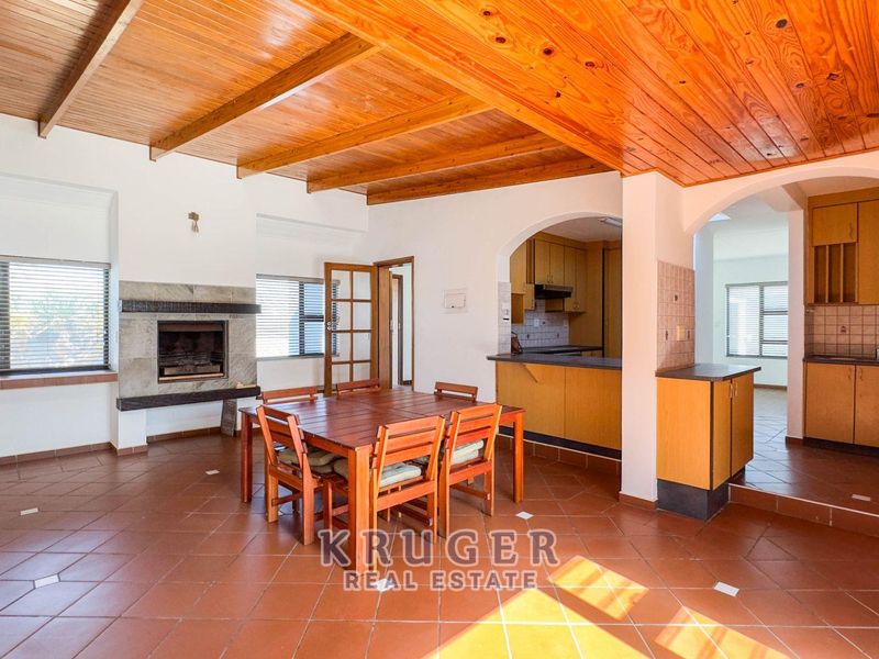 Open-plan living and dining area featuring a timber-clad vaulted ceiling, built-in fireplace, and direct access to a functional kitchen with fitted cabinetry.
