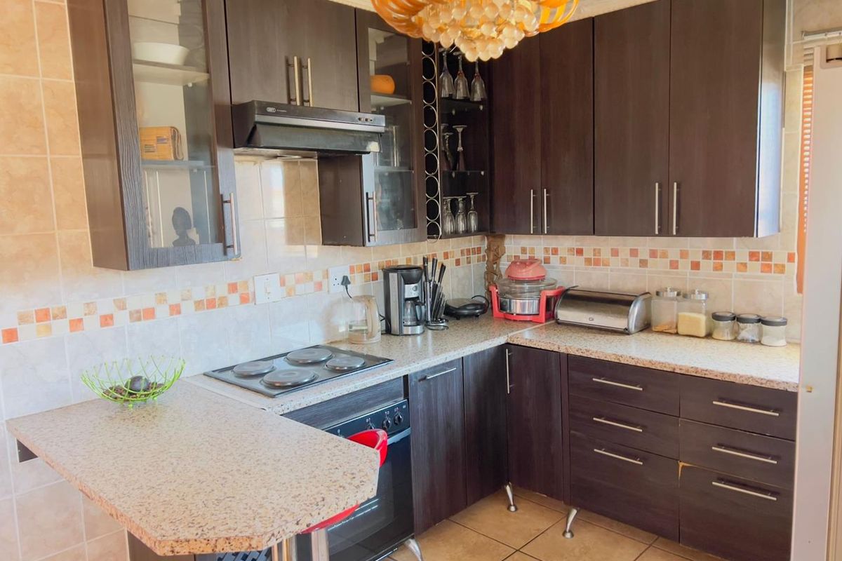 A functional kitchen featuring dark wood cabinetry, granite-look countertops, a built-in oven, electric hob, and a tiled backsplash.
