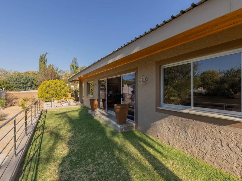Rear exterior view of the property featuring a well-maintained lawn, metal balustrade, and sliding glass doors leading into the home.