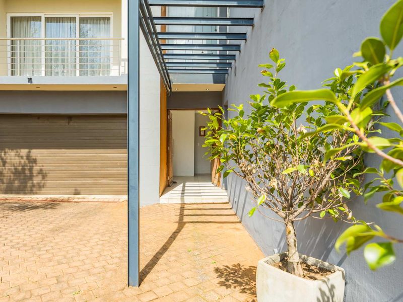 Front entrance area featuring a paved driveway, integrated garage, and a modern metal pergola leading to the main doorway.