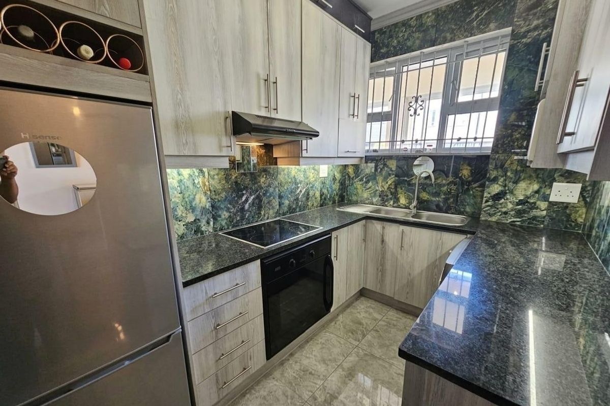 Modern kitchen featuring light wood-grain cabinetry, dark granite countertops, integrated appliances, and a striking green marble-effect tiled splashback.