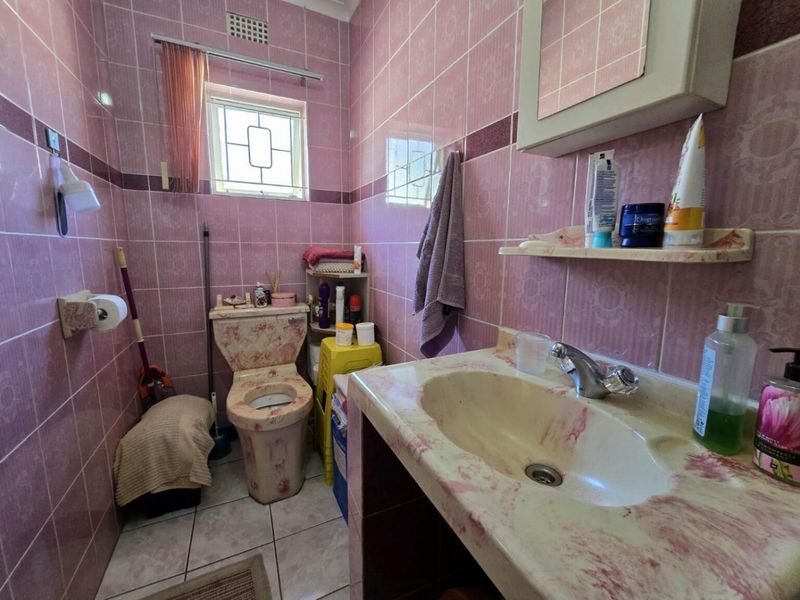 A compact bathroom featuring dated pink patterned tiling, a matching toilet, and a built-in vanity basin with storage.