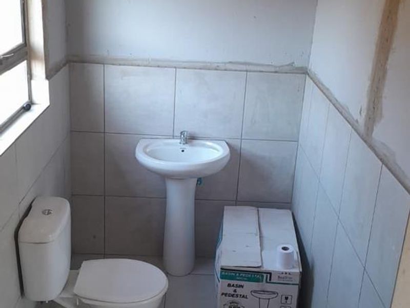A bathroom in the process of renovation, featuring a pedestal basin and toilet with partially tiled walls and unfinished plasterwork.