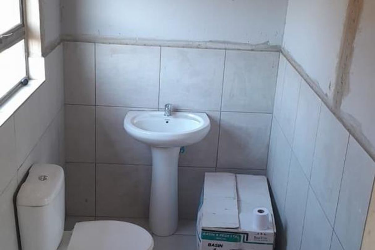 A bathroom in the process of renovation, featuring a pedestal basin and toilet with partially tiled walls and unfinished plasterwork.