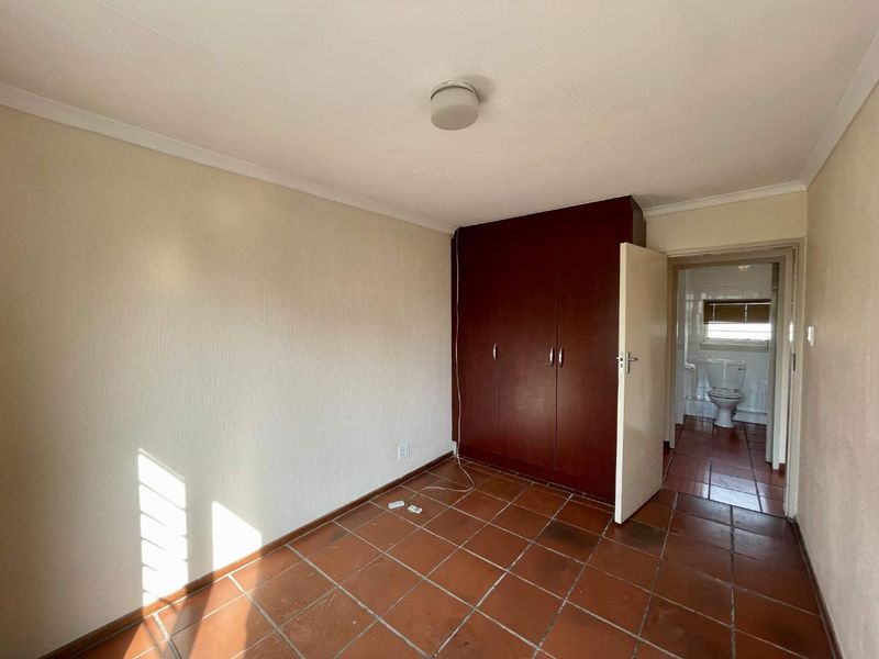 An empty bedroom featuring terracotta floor tiles, a built-in wardrobe, and direct access to an en-suite bathroom.