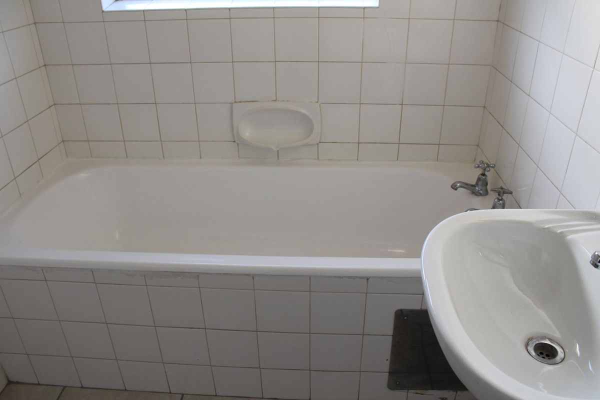 A dated bathroom featuring a standard bathtub, pedestal basin, and white ceramic wall tiles, requiring cosmetic updates to improve its overall condition.