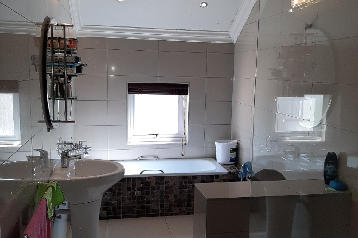 A modern bathroom featuring a pedestal basin, built-in bathtub with mosaic tile surround, glass shower enclosure, and polished floor tiles.