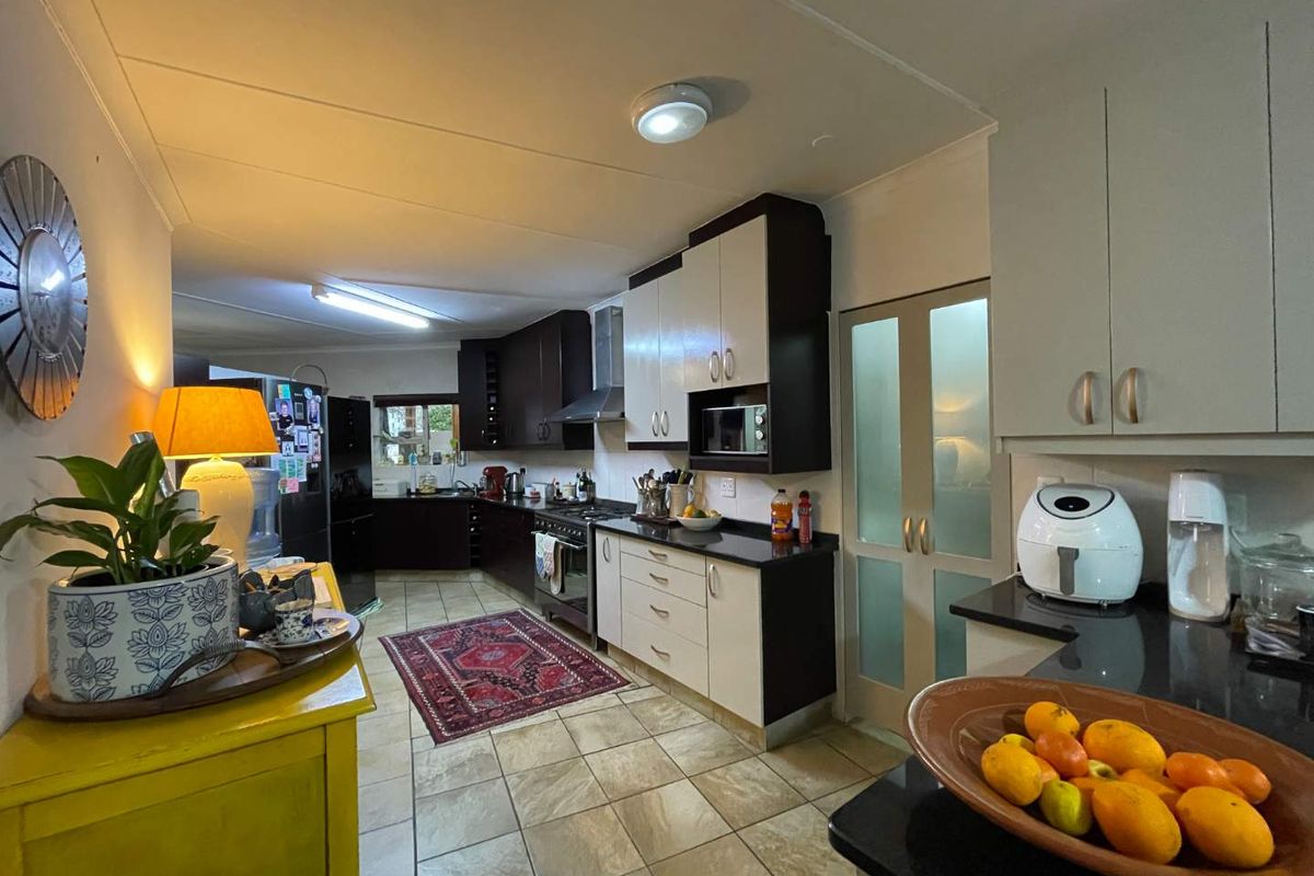 A functional kitchen featuring two-tone cabinetry, granite countertops, a gas hob, and a dedicated pantry area with frosted glass doors.