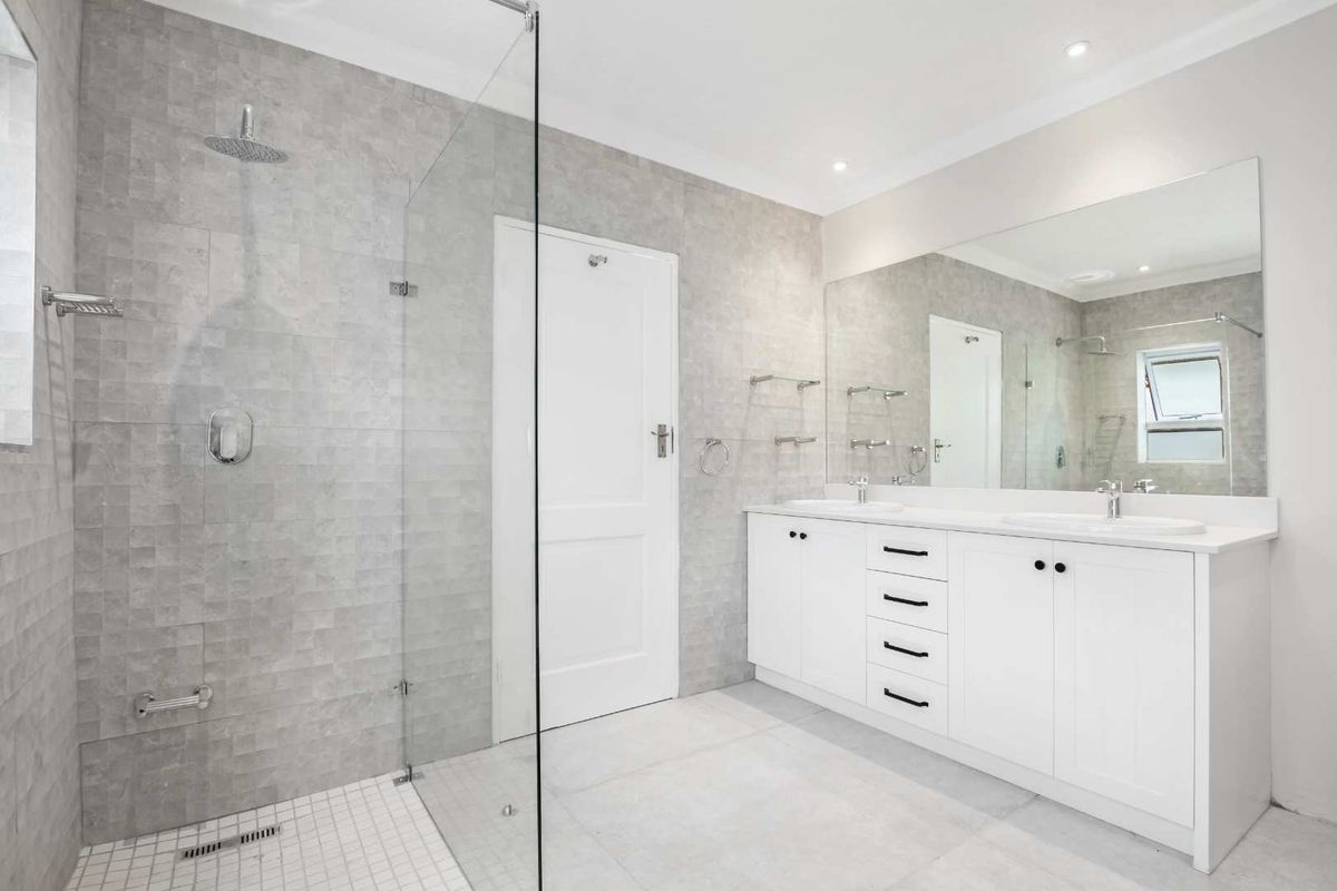 Modern bathroom featuring a spacious walk-in glass shower, dual vanity with white cabinetry, and large wall-to-wall mirror with recessed lighting.