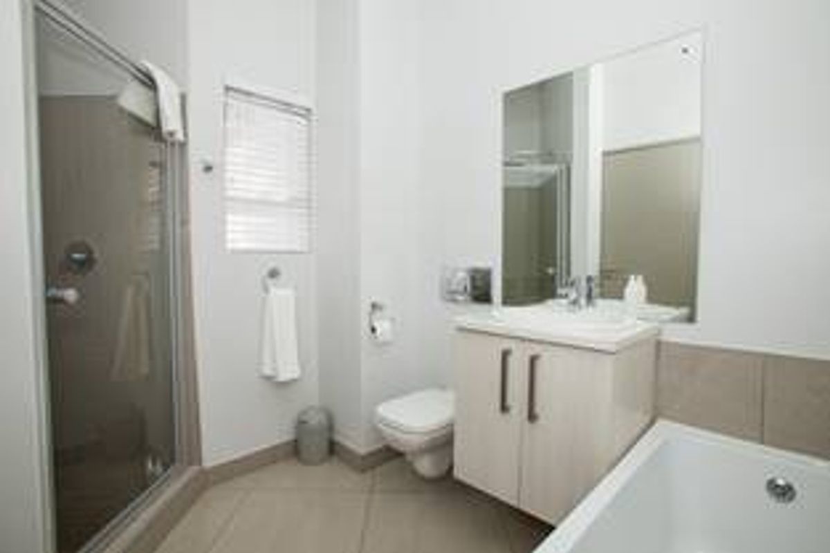A clean, modern bathroom featuring a glass-enclosed shower, a separate bathtub, a vanity with a basin, and a wall-mounted toilet.