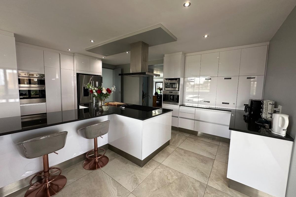 Modern kitchen featuring high-gloss white cabinetry, black stone countertops, a central island with breakfast bar, and integrated stainless steel appliances.