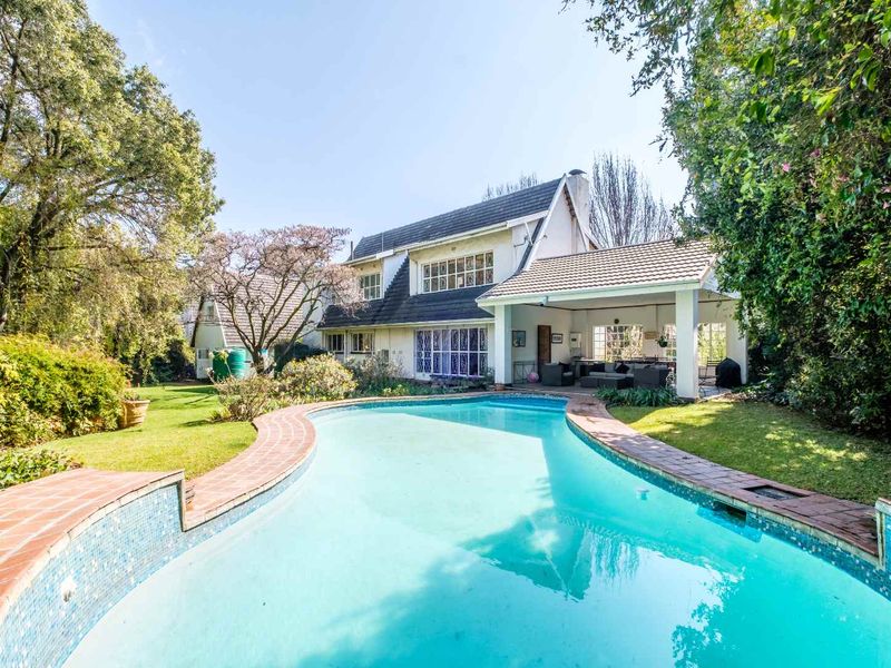 A spacious backyard featuring a swimming pool with brick coping, a covered patio area, and a well-maintained garden setting.