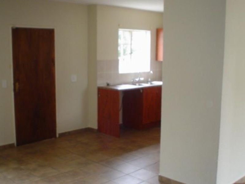 An empty kitchen area featuring built-in wooden cabinetry, tiled flooring, and a functional sink with a tiled splashback.