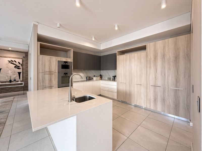 Modern kitchen featuring a central island with stone countertop, integrated cabinetry, built-in appliances, and sleek tiled flooring in a contemporary open-plan layout.