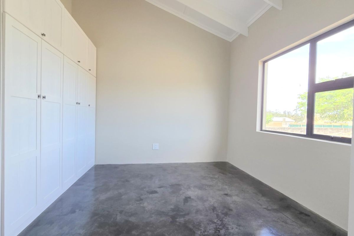 A bright, empty bedroom featuring polished concrete flooring, high vaulted ceilings, and extensive built-in white cabinetry.