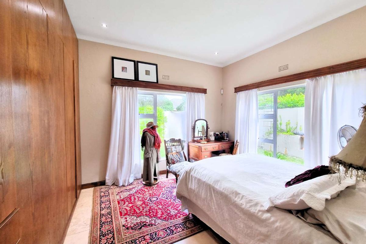 A well-lit bedroom featuring extensive built-in wooden cabinetry, tiled flooring, and large windows providing natural light and garden views.