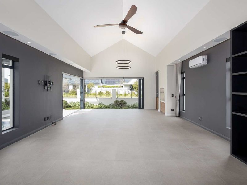 Spacious, modern living area featuring a high vaulted ceiling, large format floor tiles, built-in shelving, and seamless access to the outdoor patio area.