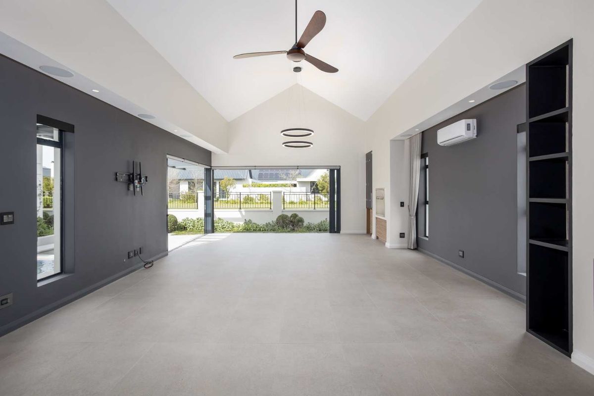 Spacious, modern living area featuring a high vaulted ceiling, large format floor tiles, built-in shelving, and seamless access to the outdoor patio area.