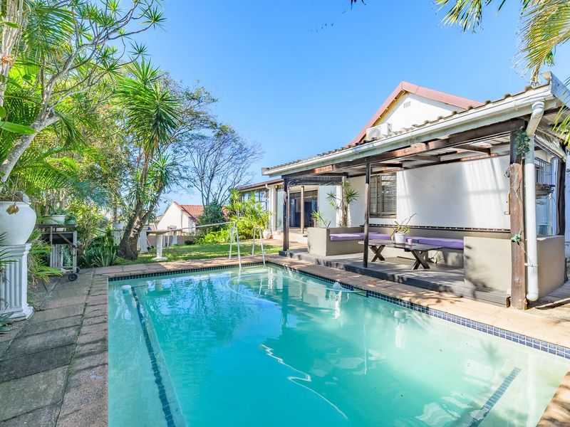 Outdoor pool area featuring a swimming pool with paved surround and an adjacent covered patio with a timber pergola and built-in seating.