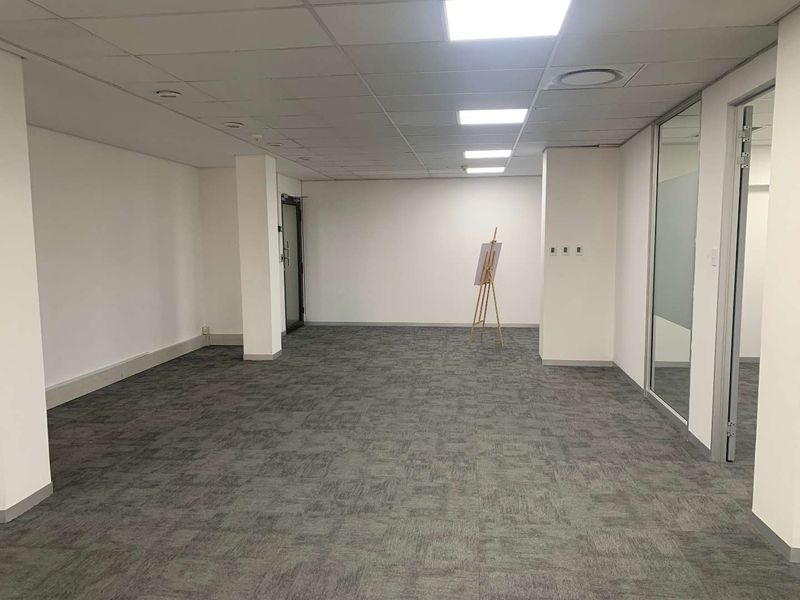A spacious, empty office area featuring neutral carpet tiles, a suspended ceiling with recessed LED lighting, and a modern glass partition wall.