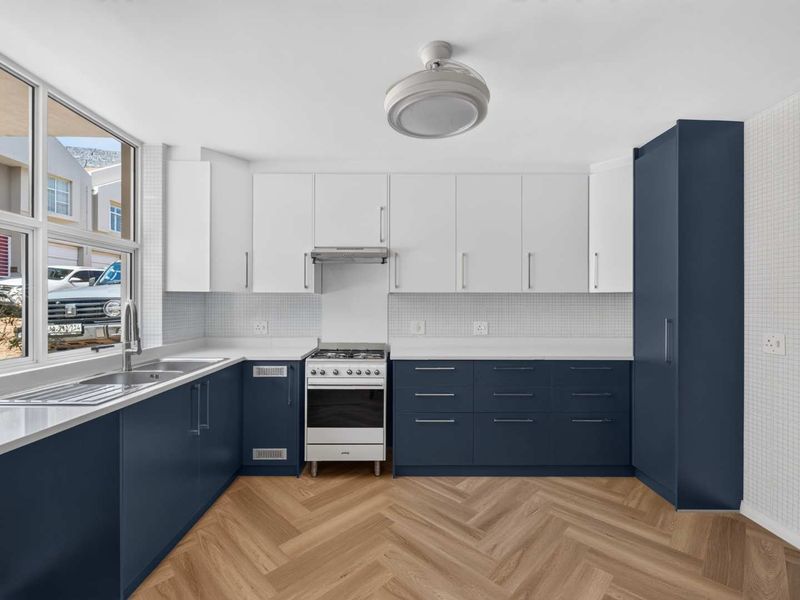 A modern, well-lit kitchen featuring navy and white cabinetry, a gas stove, stainless steel sink, and stylish herringbone flooring.