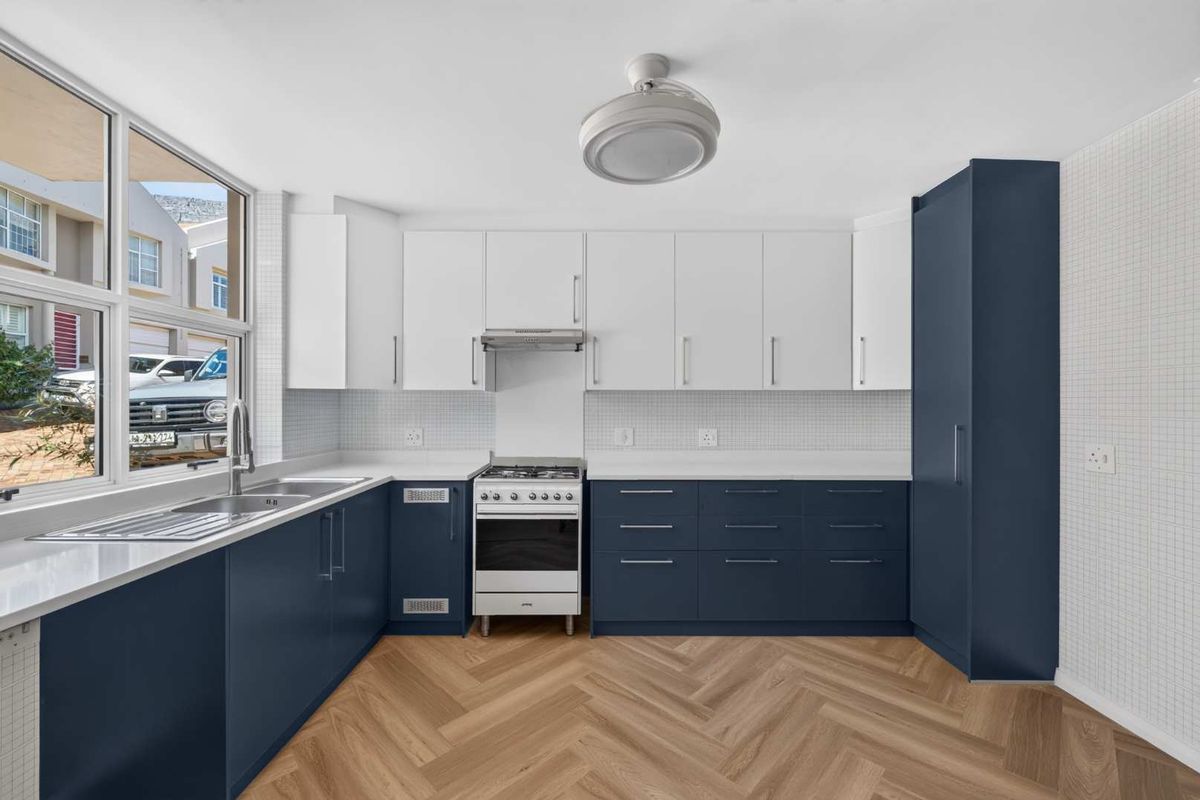 A modern, well-lit kitchen featuring navy and white cabinetry, a gas stove, stainless steel sink, and stylish herringbone flooring.