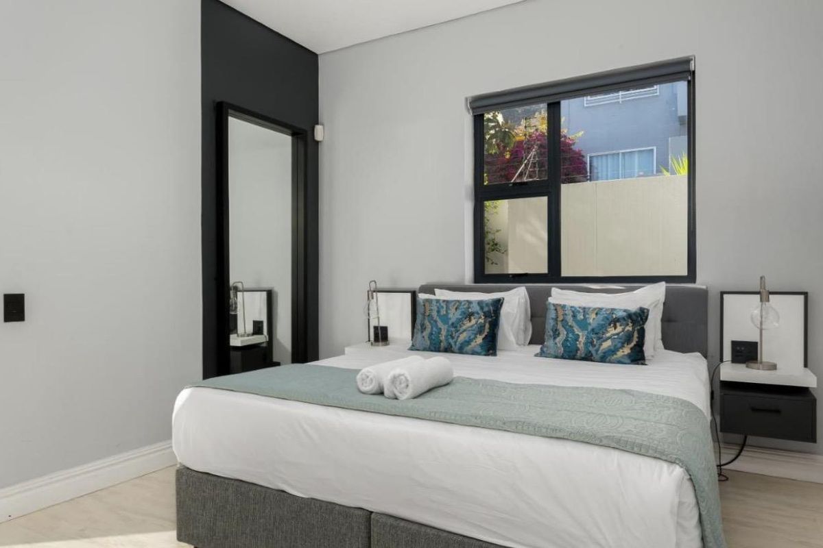 A modern bedroom featuring neutral walls, a large window with aluminium frames, and integrated bedside shelving units.