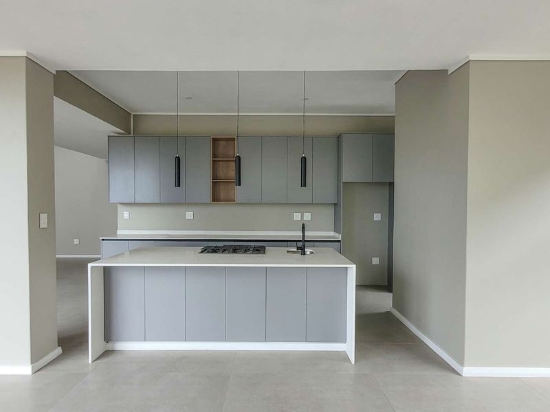 Modern kitchen featuring a central island with stone countertops, gas hob, integrated cabinetry, and sleek pendant lighting in an open-plan layout.