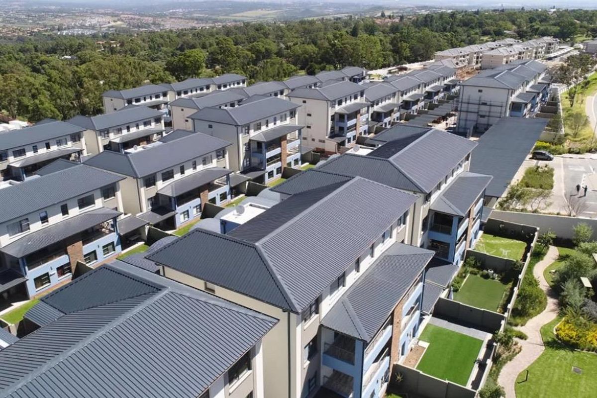 Aerial view of a modern residential apartment complex featuring multiple blocks with pitched metal roofs, landscaped grounds, and paved pathways.