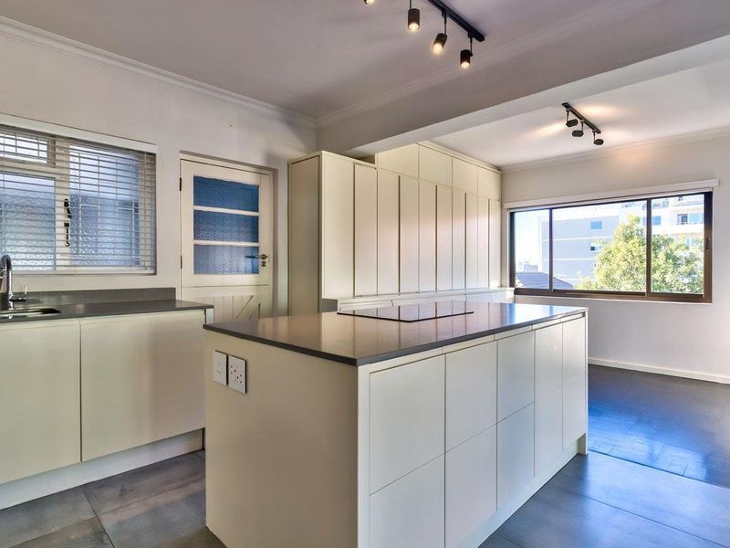 A modern, bright kitchen featuring a central island with a built-in cooktop, ample cabinetry, and sleek finishes in an open-plan layout.