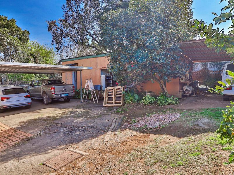 Rear exterior view of the property featuring a carport, concrete driveway, and established garden area with mature trees.