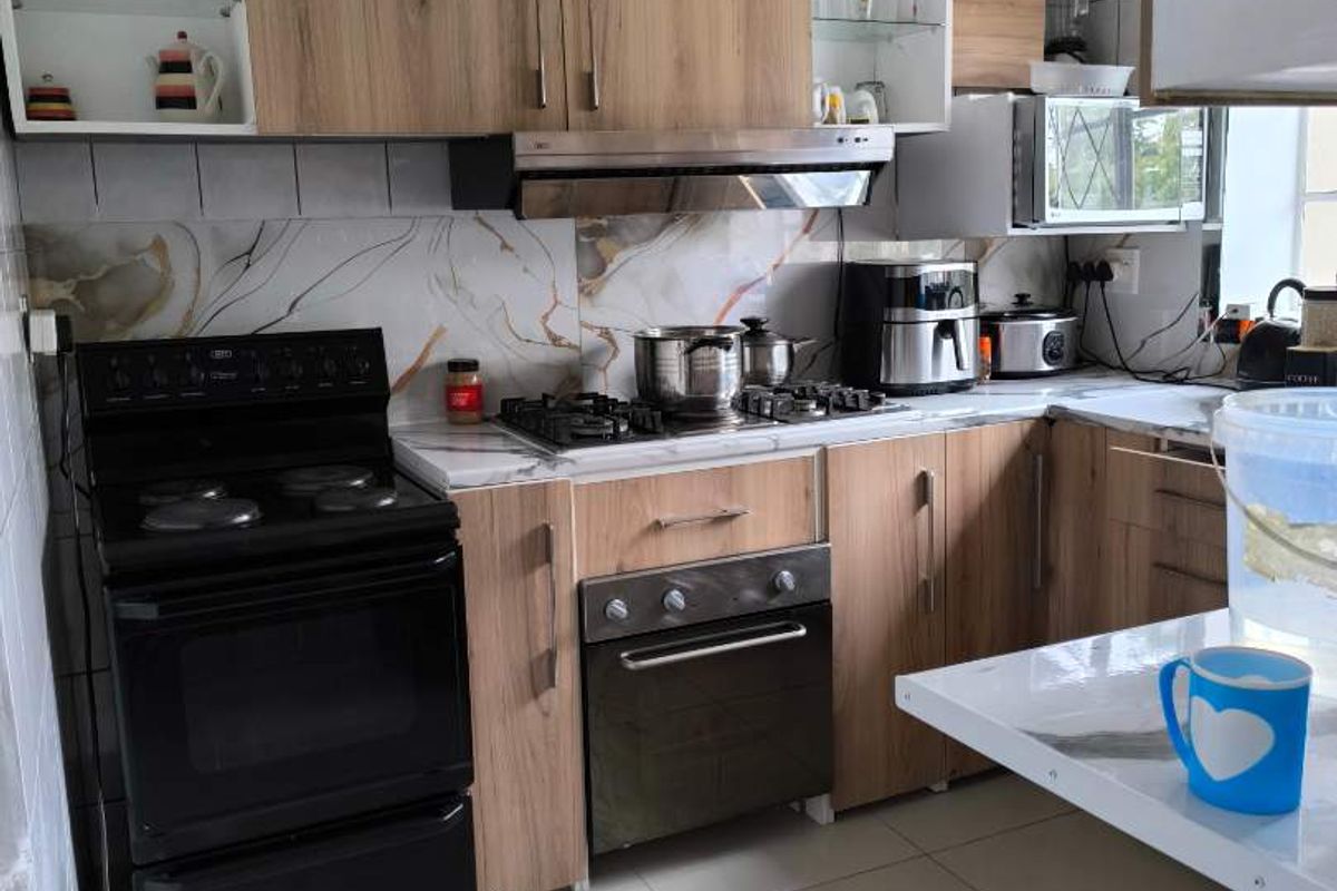 A functional kitchen featuring wood-look cabinetry, marble-effect splashback, built-in oven, gas hob, and extractor fan with tiled flooring.