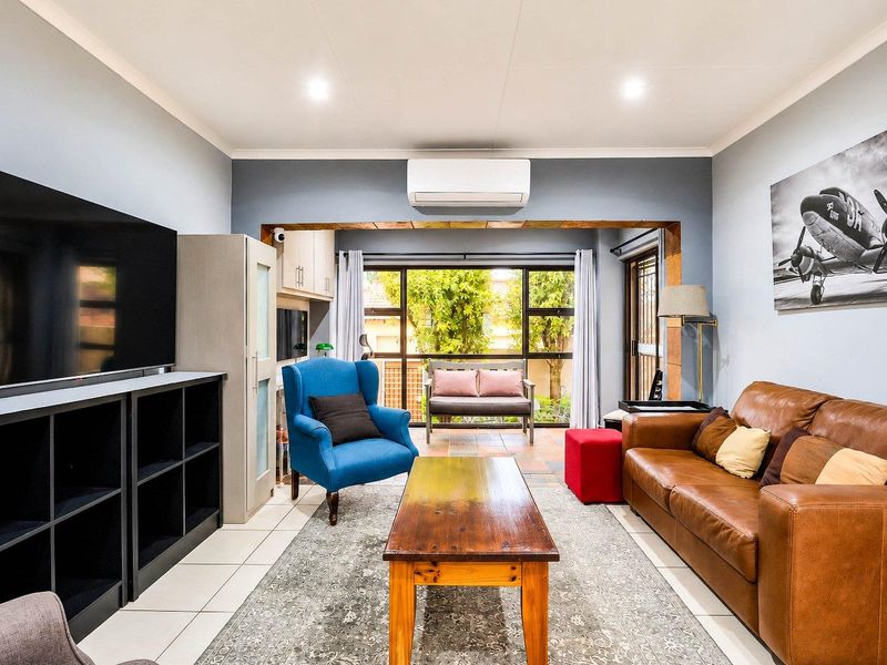 A well-lit living room featuring tiled flooring, a split-system air conditioner, and built-in cabinetry, with large windows providing natural light and garden views.