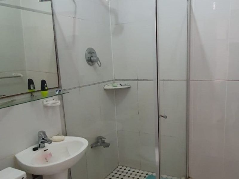 A functional bathroom featuring a pedestal basin, a glass-enclosed shower, and tiled finishes throughout.