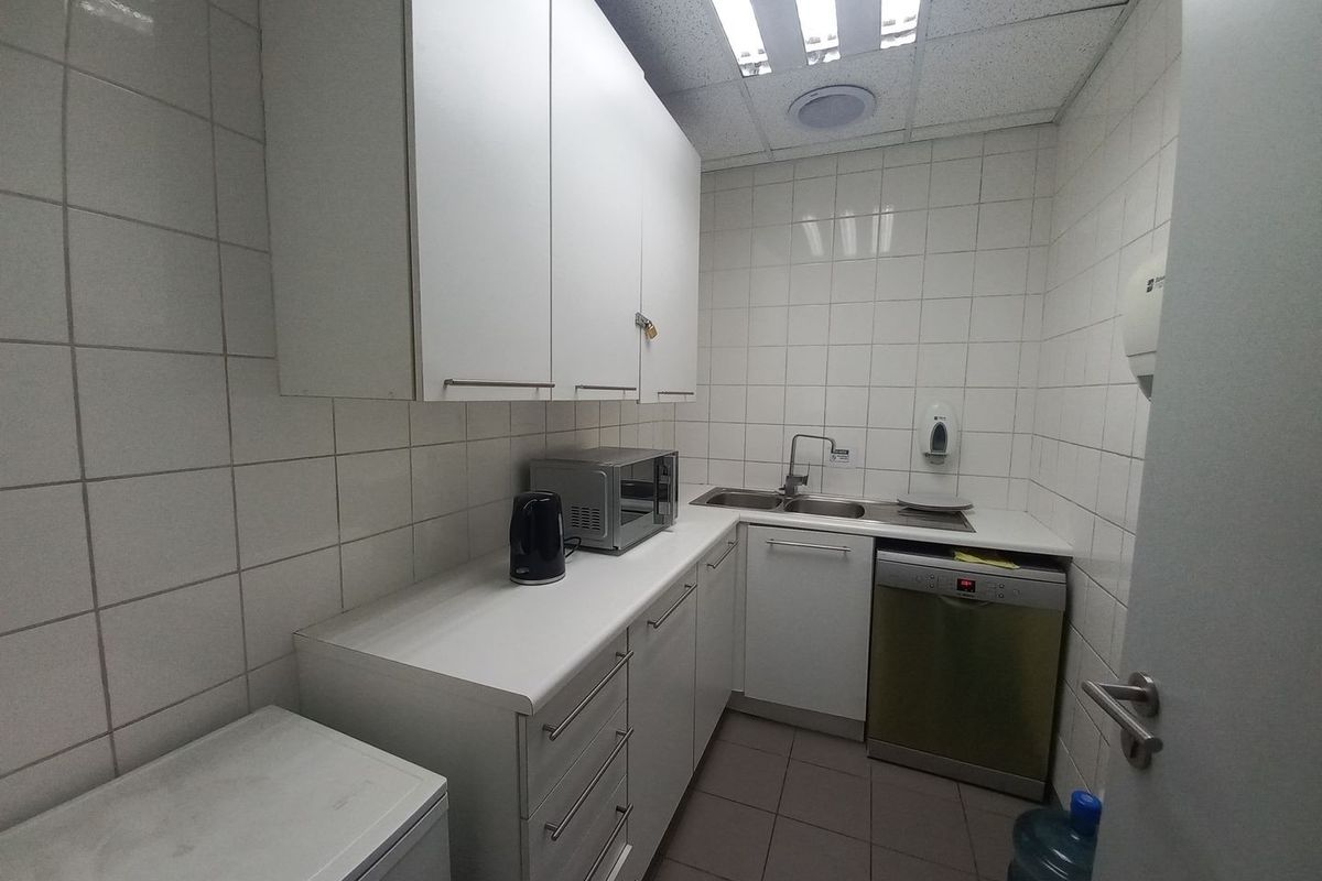 A functional industrial kitchenette featuring white cabinetry, tiled walls, a stainless steel sink, and integrated dishwasher space.