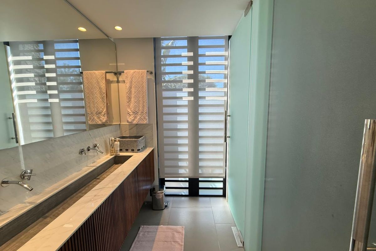 Modern bathroom featuring a sleek integrated stone vanity with dual wall-mounted faucets, large mirror, and frosted glass privacy door.