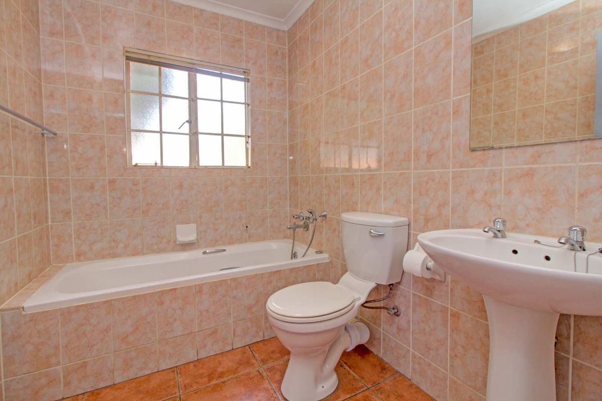 A functional bathroom featuring a built-in bathtub, pedestal sink, and toilet, finished with dated wall and floor tiles.